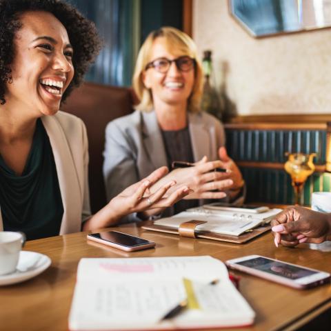 Three people laugh over a lunch meeting